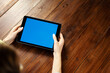 © Rymden - Mockup image of a woman using digital tablet with blank screen on wooden table. Close up photo of female hands holding device horizontally