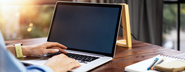 Mockup image of a woman using laptop with blank screen on wooden table