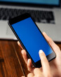 © Rymden - Mockup image of a woman using smartphone with blank screen on wooden table. Close up photo of female hands holding mobile phone vertically