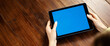 © Rymden - Mockup image of a woman using digital tablet with blank screen on wooden table. Close up photo of female hands holding device horizontally