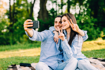 Wall Mural - Young loving couple lie on a plaid in the park and use the phone, beautiful guy and girl