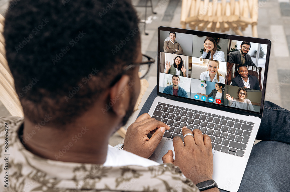 Video call. Video conference. Successful African American freelancer communicate by a video conference with his colleagues using a laptop while sitting in cafe in a summer terrace - obrazy, fototapety, plakaty 