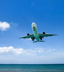 a passenger plane lands low over the sea, at an airport near the beach on a Sunny day