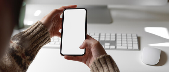 Female employee looking information on mock-up smartphone while working at office desk