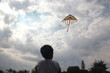 niño latino jugando vuela papalote en cielo con nubes y sol brillante 