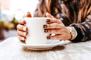 Wall Mural - woman hand holding a cup of coffee outdoors at coffee shop or cafe with blurred background