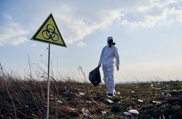 focus on biohazard warning sign. on blurred background ecologist in suit and gas mask holding garbag