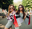 © Вячеслав Косько - Beautiful smiling girls walking at park after shooping and big sales with many papers bags in hands. Women in glasses with red lips, fashionable wearing in dresses and sunglasses. Summertime.