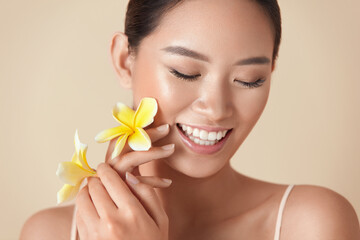 Wall Mural - beauty. model with flower portrait. happy ethnic woman with exotic plumeria near face against beige 