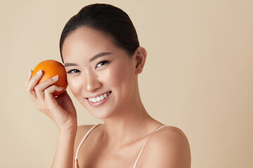 Wall Mural - face. woman and fruit beauty portrait. smiling asian model with orange looking at camera against bei