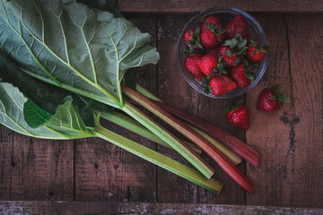 Rhubarb stems and strawberries on a dark garden table