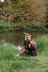 Wall Mural - Stylish model girl in clothes on the grass near the small river reeds trees