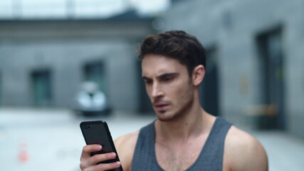 Closeup athlete man looking smartphone on street. Smiling man reading message