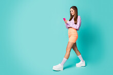 Full Body Profile Photo Of Cool Lady Youth Outfit Hold Telephone Hands Walk Street Read Sms Wear Purple Cropped Sweater Orange Skirt Shoes Long Socks Isolated Teal Color Background