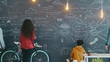 Time Lapse Of Creative Youth Coworkers Writing And Drawing On Black Chalkboard Indoors In Open Space Office Room. Project, Creativity And Workplace Concept.