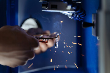 Closeup of man's hands repairing eyeglasses frame with laser welding machine in optical workshop. Glasses repair, professional manufacturing, laser soldering