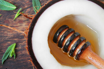 
honey dipper with liquid natural honey served in, sliced ​​coconut on a wooden plate with fresh mint leaves.