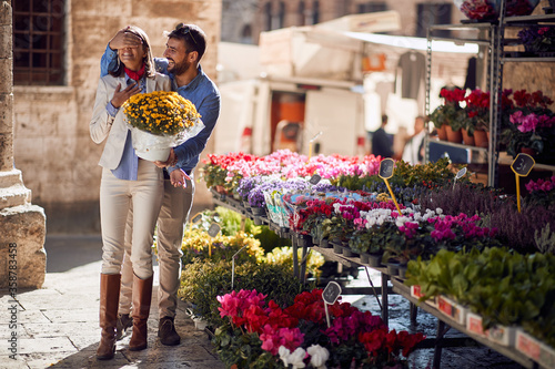 Fotografía man is surprising female with a bouquet of flowers holding her eyes closed in front of a flower shop