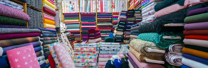 clothes in shop, rolls of fabric and textiles for sale stacked on shelves in shop, view of cloth rol