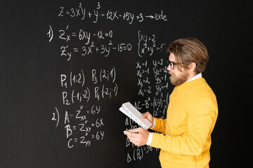 Bearded teacher in casualwear rewriting formulas on blackboard from his copybook