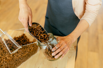 Wall Mural - Dark brown whole grains of pasta are poured in glass jar. Close up of unrecognizable woman pouring pasta from plastic free packaging paper bag into storage jar.