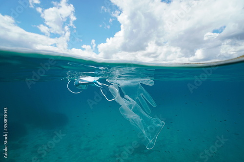 Plastic waste pollution in the sea since coronavirus COVID-19 pandemic, face mask with gloves underwater and sky with cloud, split view over and under water surface