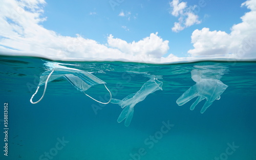Plastic waste pollution underwater since coronavirus COVID-19 pandemic, face mask with gloves in the ocean and blue sky with cloud, split view over and under water surface