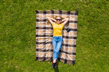 Aerial View Of Young Woman Lying On Her Back On The Towel And Green Grass.