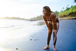 © BullRun - Cheerful athletic afro american jogger dressed in tracksuit has break during morning run along seashore.Positive female with dark skinned happy after hard sport workout on coastline of tropical island