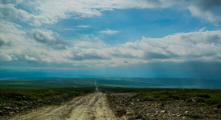 gravel road to mountain ridge with small coniferous trees during stormy weather with gray clouds