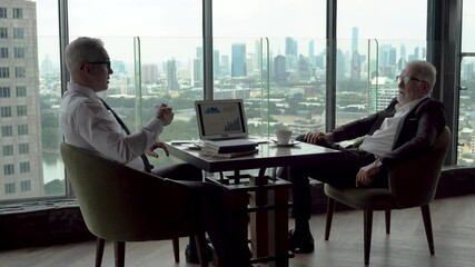 Wall Mural - two senior businessman take a break drinking coffee and discussing business strategy on table with graph in laptop computer in coffee shop at modern restaurant on a tall building cityscape background