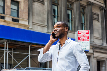 Young African American Man with beard traveling in New York City, wearing white long sleeve shirt,  walking on street in Midtown of Manhattan, looking up, talking on cell phone..