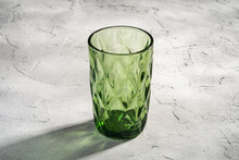Green Glass Geometric Cup With Colorful Shadow Light Rays On Stone Concrete Background, Angle View