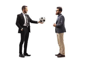 Man in a suit giving a soccer ball to a bearded man