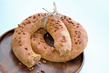 Composition of two homemade bagels (one piece broken off) with pine nuts tied with a rope on a dark wood plate