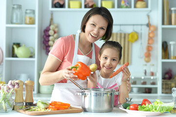 Wall Mural - Cute little girl with mother cooking soup together at kitchen table