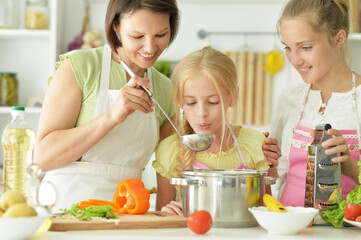 Wall Mural - Cute girls with mother preparing delicious fresh salad in kitchen