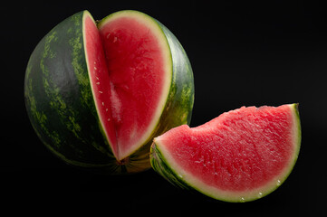 Fresh fruit dessert and delicious food concept with low key high contrast moody picture of seedless watermelon next to a red juicy slice isolated on black background with clipping path cutout