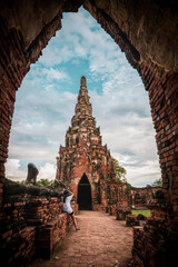 Wall Mural - A tourist with back to the camera takes a photograph of ancient ruins in Ayyuthaya Thailand, framed by an arch.