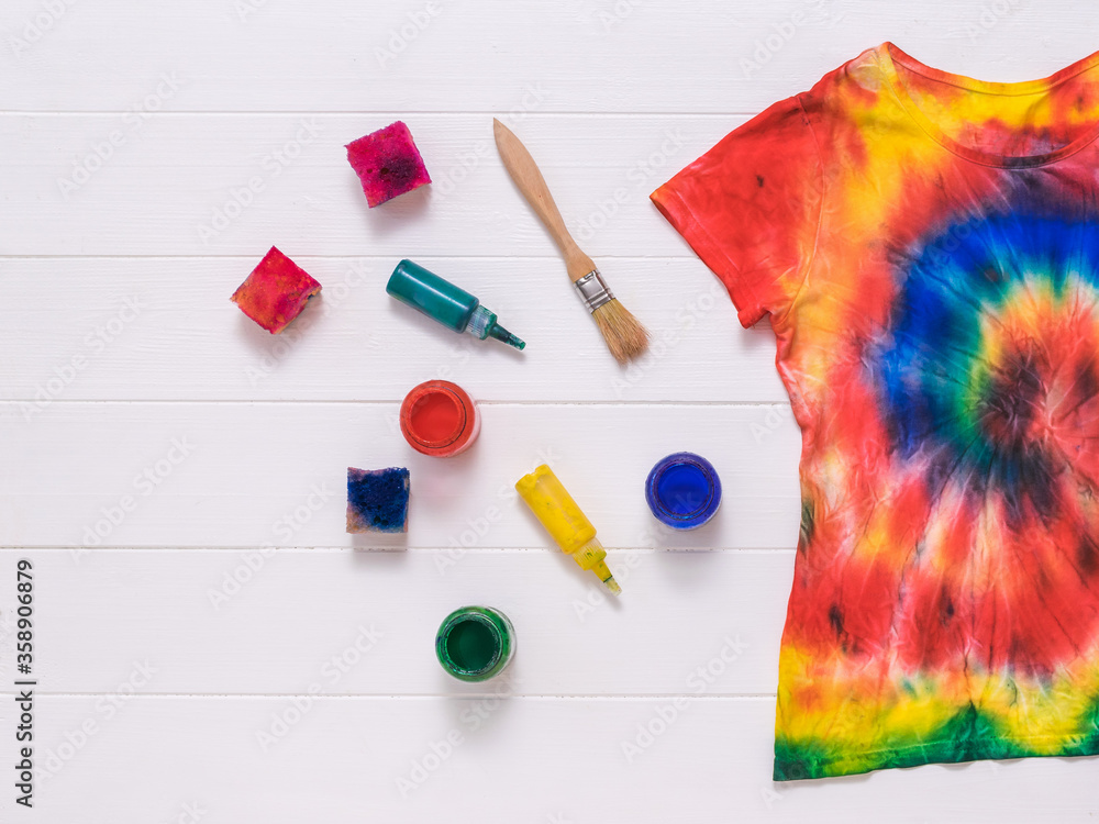 Brushes, paint, and a tie dye t-shirt on white boards. Flat lay. - obrazy, fototapety, plakaty 
