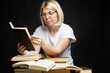 © Анна Демидова - A smiling young blonde woman reads in glasses with a bunch of books. Education, knowledge and hobbies. Black background.