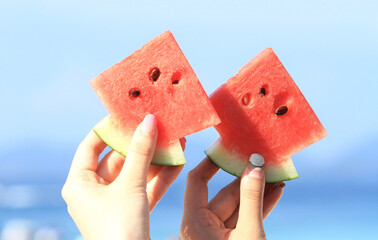 Two hands of teen girls both hold  a slice of watermelon on a  bright blue sky background