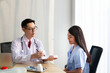 © Avirut S. - Doctor with female patient. Doctor and patient discussing something while sitting at the table, explaining diagnosis to his female patient. Medicine and healthcare concept. Coronavirus, Covid-19.