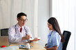 © Avirut S. - Doctor with female patient. Doctor and patient discussing something while sitting at the table, explaining diagnosis to his female patient. Medicine and healthcare concept. Coronavirus, Covid-19.