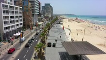 Aerial Shot Of Vehicles On Street By Buildings And Beach, Drone Flying Forward Over City Against Sky On Sunny Day - Tel Aviv, Israel