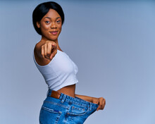 Happy Woman In White Top In Oversize Jeans Smiles And Shows Victory Gesture. Diet Concept