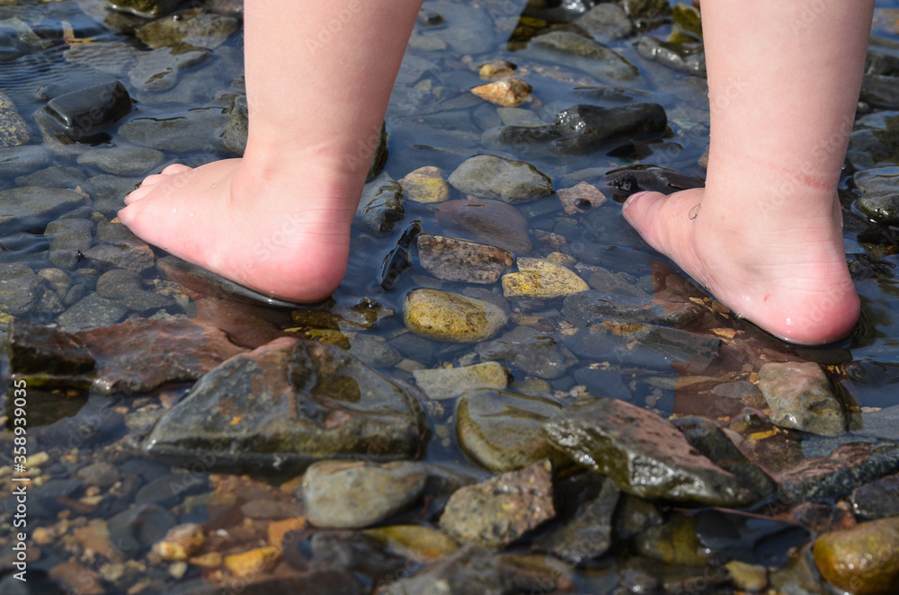 Child's feet close-up walking on water on rocks. Exercises for health ...