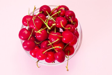 Wall Mural - glass bowl full of delicious red cherries on pink background