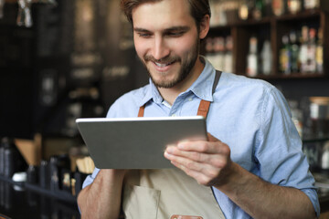 Wall Mural - Young male owner using digital tablet while standing in cafe.