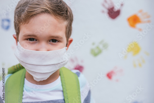 Child (5-7 years old) with mask and green backpack on a coloured background. Back to school concept